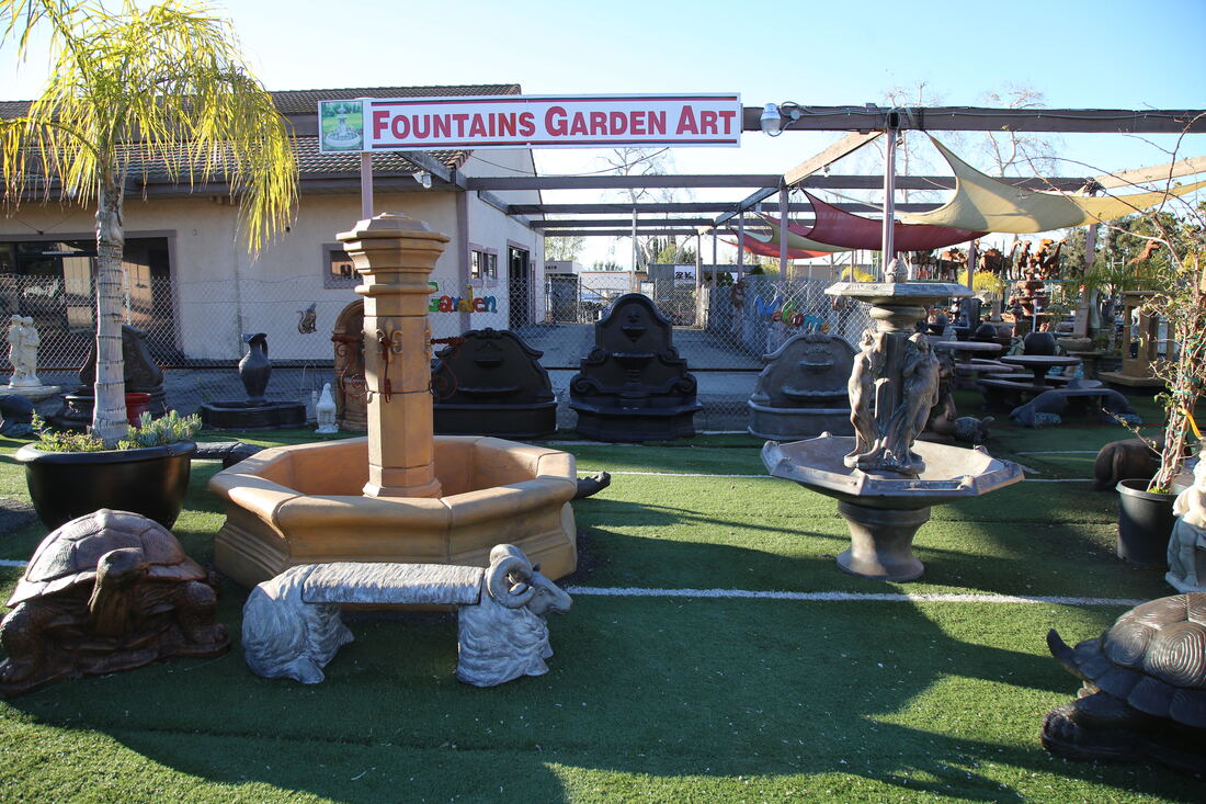 A tiered fountain running in the foreground with the Fountains Garden Art sign behind it.