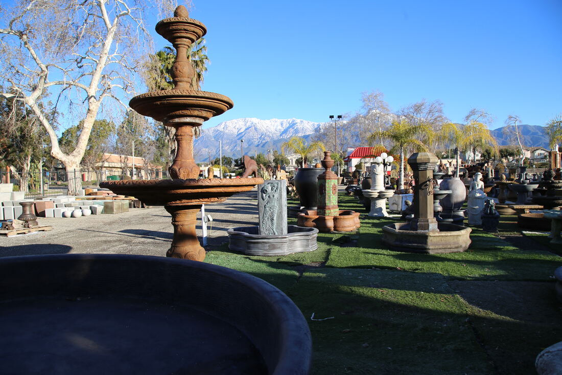 A tall two-tier terracotta fountain with the snow-capped San Gabriel Mountains behind it.