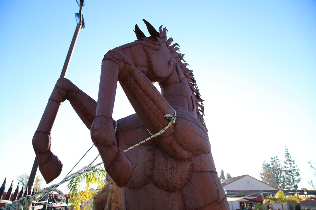 A large hand-forged metal horse sculpture standing against a clear blue sky in the yard.