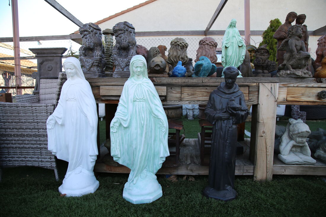 Painted devotional statues displayed on a wooden bench under the shade sails.