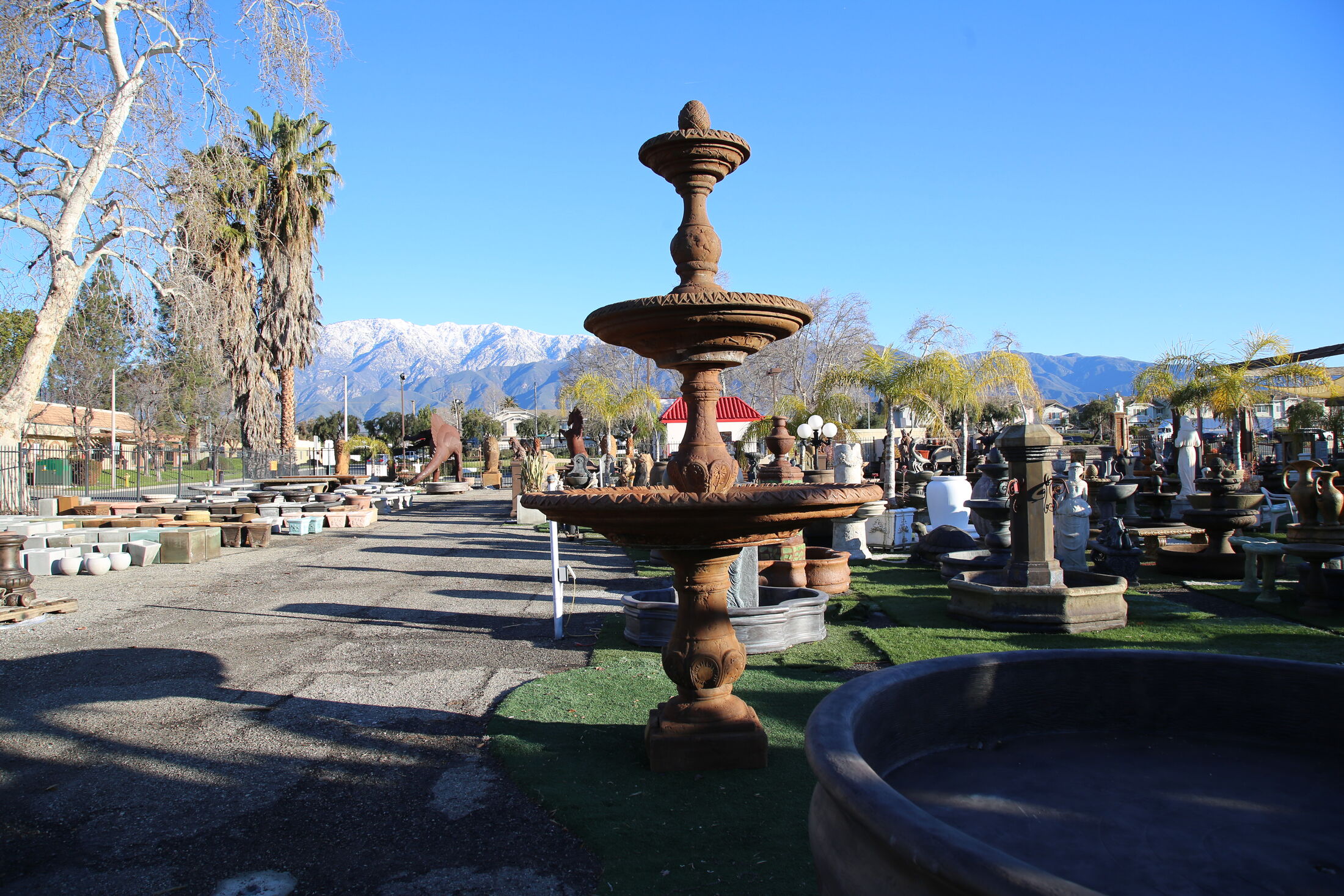 Tiered stone fountains across the Fountains Garden Art yard in Rancho Cucamonga, with the snow-capped San Gabriel Mountains behind.